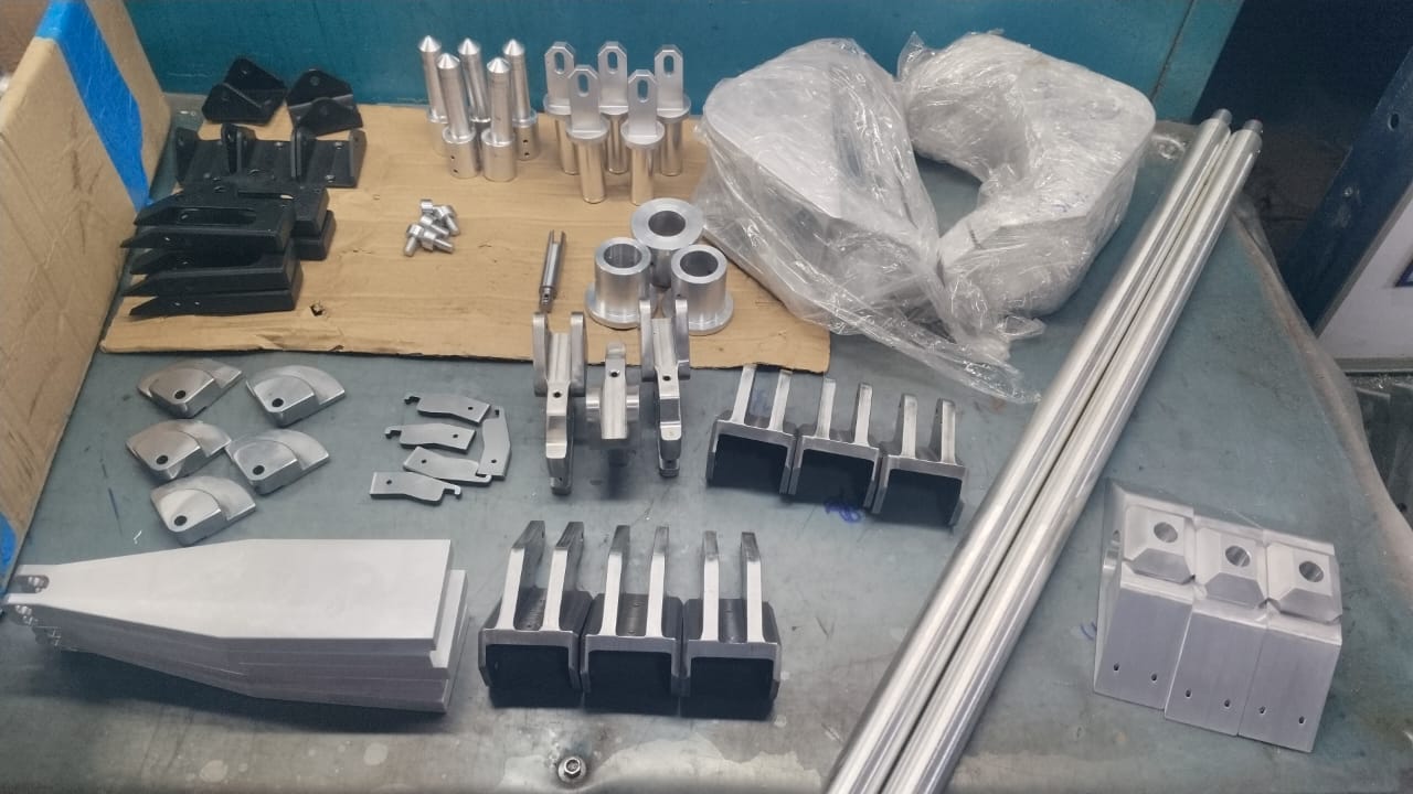 Production run on the bench — brackets, pins, channel pieces, and shafts staged for inspection